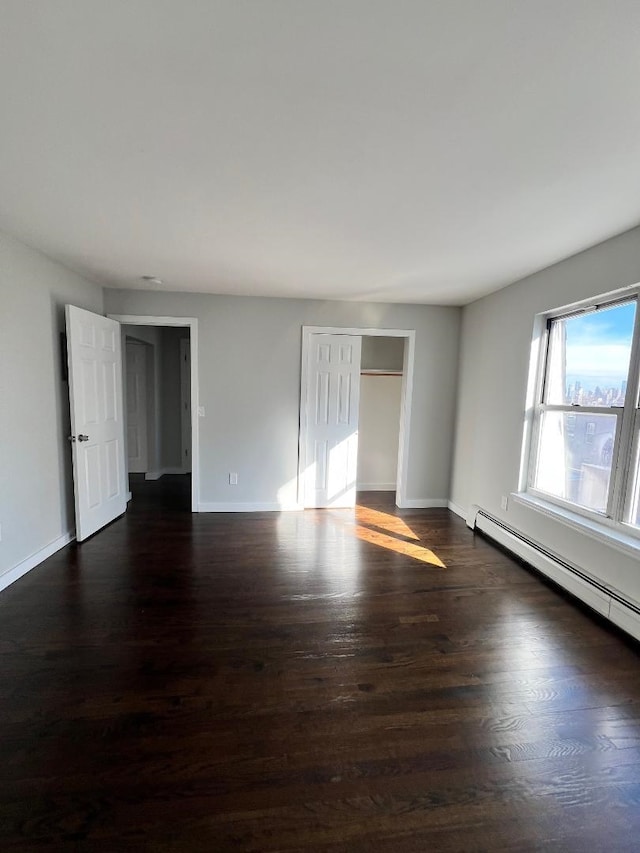 empty room featuring a baseboard heating unit and dark hardwood / wood-style floors