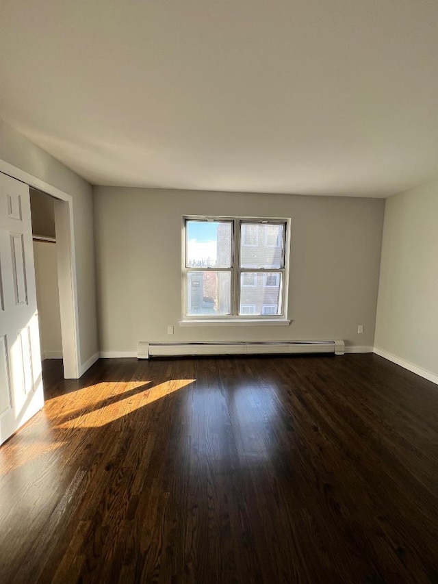 unfurnished room with dark wood-type flooring and baseboard heating