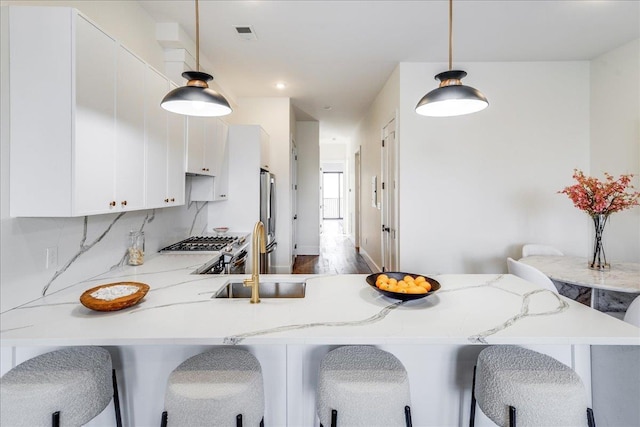 kitchen with white cabinets, a breakfast bar, sink, decorative light fixtures, and tasteful backsplash