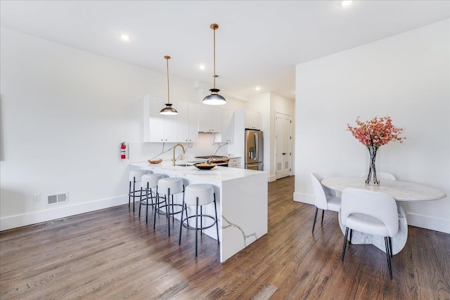 kitchen with decorative light fixtures, white cabinetry, kitchen peninsula, stainless steel refrigerator with ice dispenser, and dark wood-type flooring