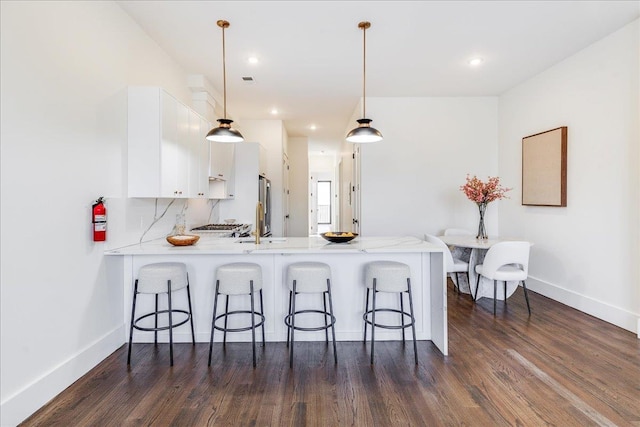 kitchen featuring white cabinets, pendant lighting, kitchen peninsula, dark hardwood / wood-style floors, and a breakfast bar