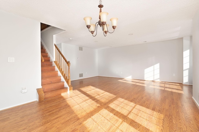 unfurnished living room featuring light hardwood / wood-style floors, a textured ceiling, and a chandelier