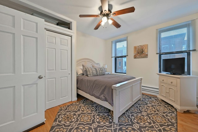 bedroom featuring a baseboard radiator, ceiling fan, light hardwood / wood-style flooring, and a closet