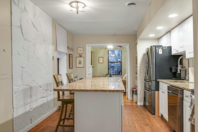 kitchen featuring white cabinets, dishwasher, light hardwood / wood-style floors, a breakfast bar area, and light stone countertops