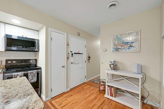 kitchen featuring stainless steel appliances, white cabinets, light hardwood / wood-style floors, and light stone counters