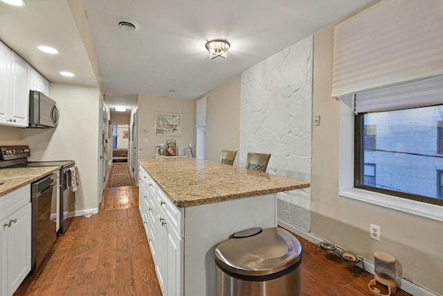 kitchen featuring appliances with stainless steel finishes, a center island, light stone counters, dark hardwood / wood-style floors, and white cabinets