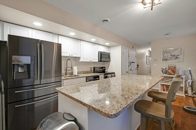 kitchen featuring light stone counters, white cabinetry, appliances with stainless steel finishes, wood-type flooring, and sink