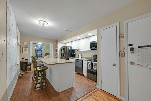 kitchen with stainless steel appliances, white cabinets, a center island, hardwood / wood-style flooring, and a breakfast bar area