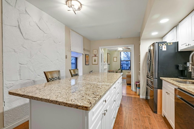 kitchen featuring a breakfast bar, a kitchen island, light wood-type flooring, white cabinets, and black dishwasher