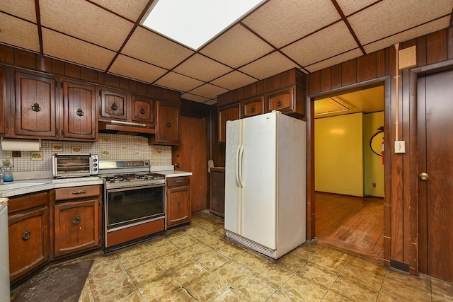 kitchen with decorative backsplash, stove, a paneled ceiling, and white fridge with ice dispenser