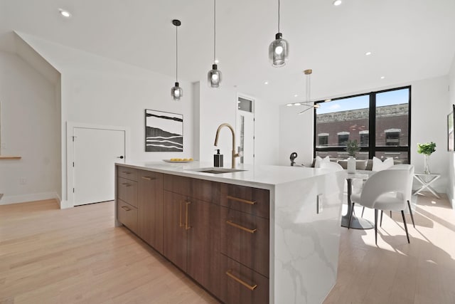 kitchen featuring pendant lighting, sink, an island with sink, expansive windows, and light wood-type flooring