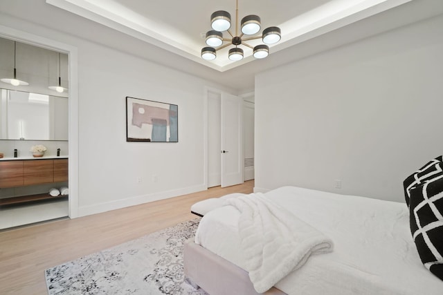 bedroom with a chandelier, connected bathroom, a raised ceiling, and light hardwood / wood-style flooring