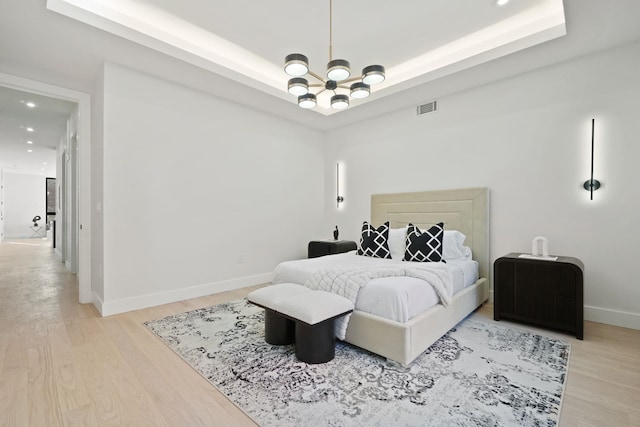 bedroom featuring an inviting chandelier, a tray ceiling, and light hardwood / wood-style floors