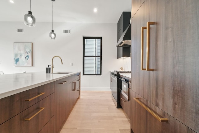 kitchen featuring stainless steel gas range, sink, light wood-type flooring, paneled refrigerator, and pendant lighting