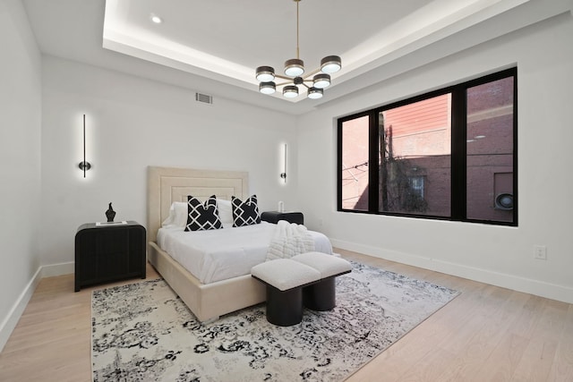 bedroom with a chandelier, light wood-type flooring, and a tray ceiling