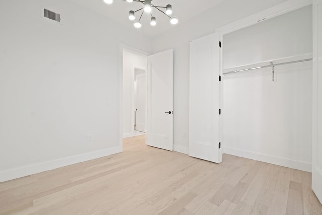 unfurnished bedroom featuring an inviting chandelier, light hardwood / wood-style floors, and a closet