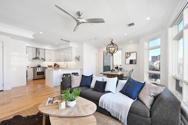 living room with visible vents, crown molding, light wood-type flooring, recessed lighting, and ceiling fan with notable chandelier