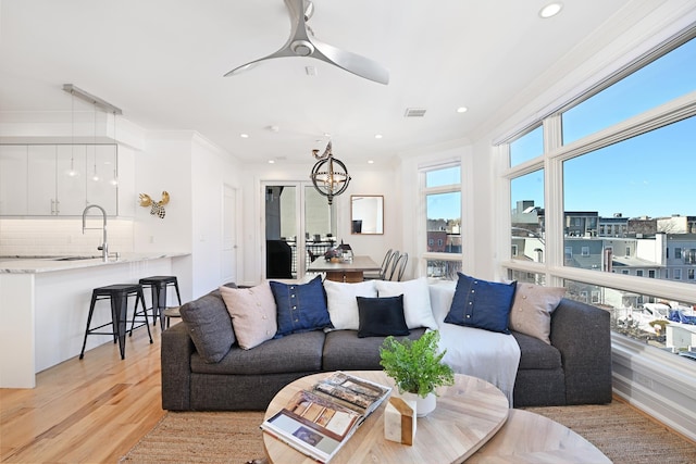 living room with light wood finished floors, visible vents, ornamental molding, ceiling fan with notable chandelier, and recessed lighting