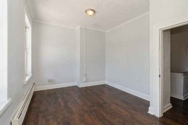 empty room featuring baseboards, a baseboard radiator, ornamental molding, and wood finished floors