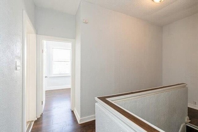 hallway featuring baseboards, an upstairs landing, and dark wood-type flooring