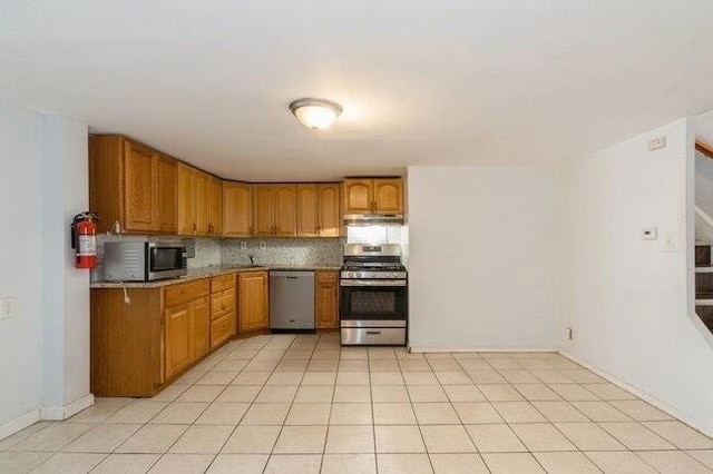 kitchen featuring under cabinet range hood, brown cabinetry, appliances with stainless steel finishes, and decorative backsplash