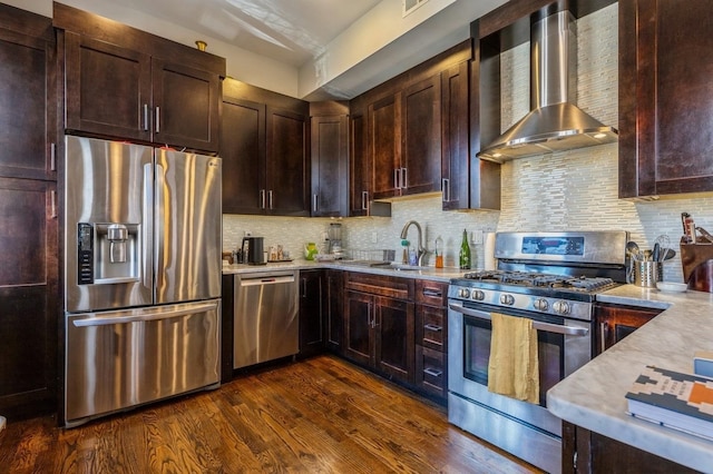 kitchen with wall chimney exhaust hood, appliances with stainless steel finishes, dark wood-style flooring, a sink, and backsplash