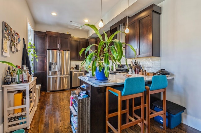 kitchen with dark brown cabinetry, decorative backsplash, appliances with stainless steel finishes, dark wood-type flooring, and hanging light fixtures