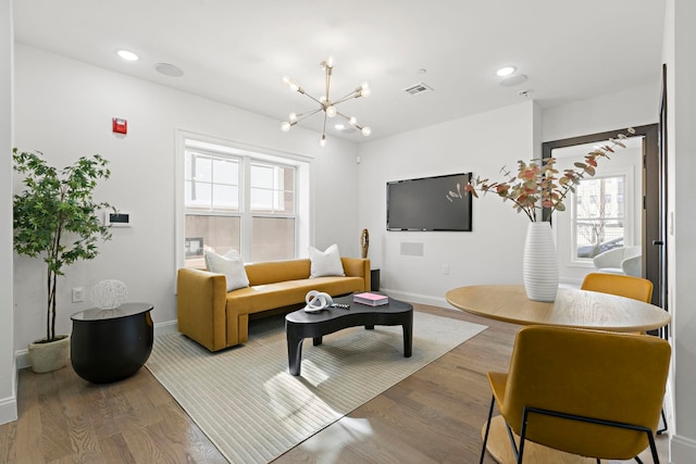 living area featuring a notable chandelier, plenty of natural light, visible vents, and wood finished floors