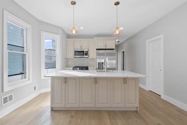 95 Claremont Ave, Jersey City, NJ 07304 - kitchen featuring appliances with stainless steel finishes, light wood finished floors, cream cabinets, an island with sink, and tasteful backsplash