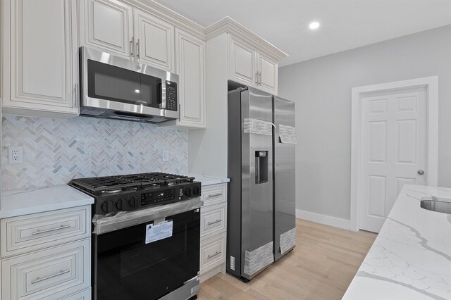 95 Claremont Ave, Jersey City, NJ 07304 - kitchen with appliances with stainless steel finishes, tasteful backsplash, light stone counters, light wood-style floors, and white cabinets
