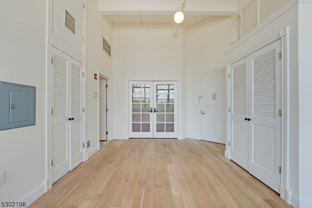 hall with beam ceiling, french doors, a high ceiling, and electric panel