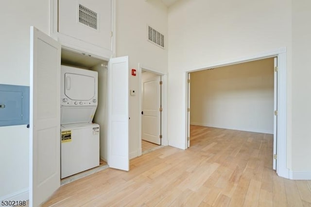 clothes washing area featuring light wood-type flooring, stacked washer and clothes dryer, a high ceiling, and electric panel