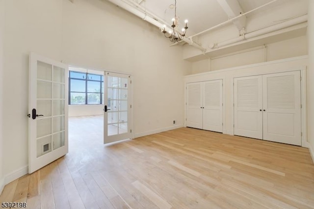 interior space featuring two closets, a towering ceiling, french doors, a chandelier, and light hardwood / wood-style flooring