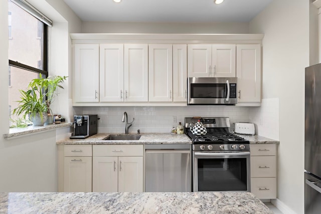 263 10th St Unit 2D, Jersey City, NJ 07302 - kitchen featuring appliances with stainless steel finishes, a sink, tasteful backsplash, white cabinets, and light stone counters