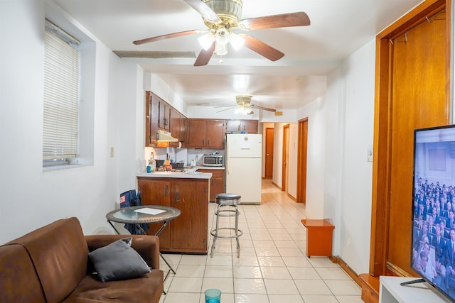 kitchen with stainless steel microwave, a peninsula, freestanding refrigerator, a ceiling fan, and light tile patterned floors