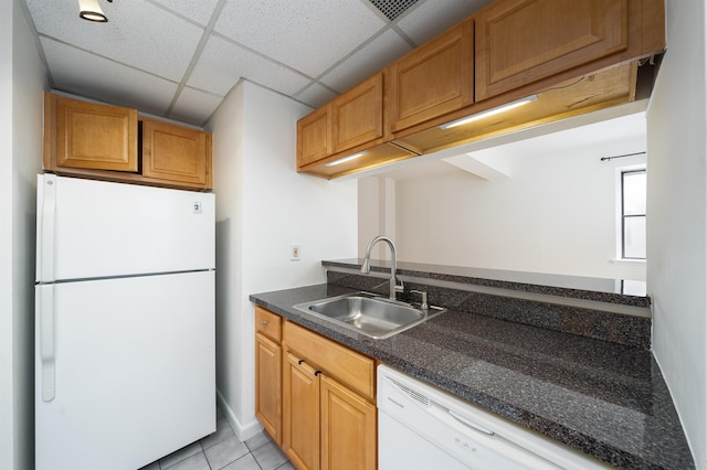 kitchen featuring white appliances, dark stone countertops, sink, light tile patterned flooring, and a drop ceiling