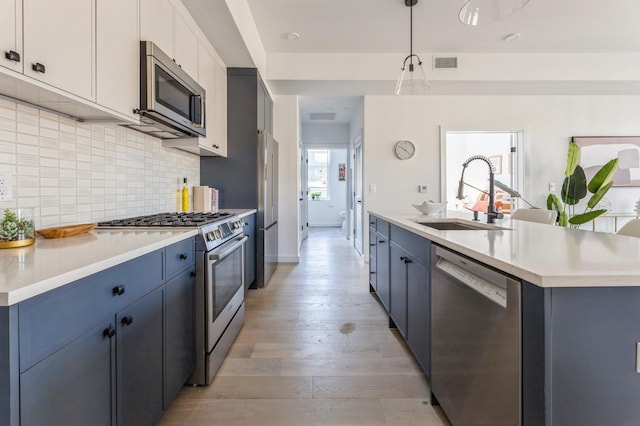 kitchen featuring sink, hanging light fixtures, stainless steel appliances, an island with sink, and white cabinets