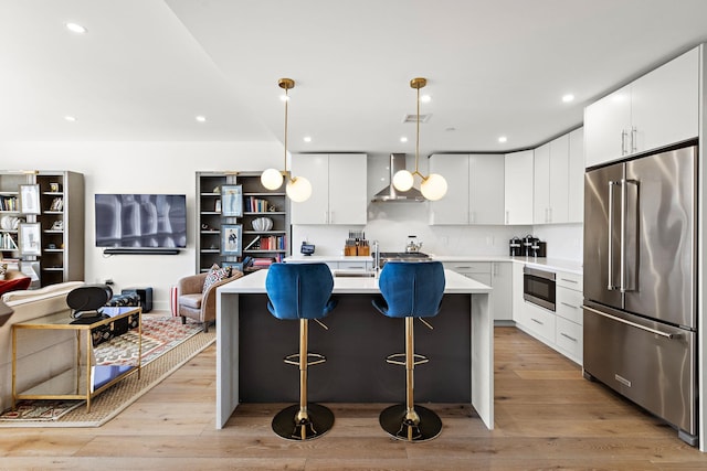 kitchen with light wood-style floors, a kitchen breakfast bar, wall chimney range hood, light countertops, and stainless steel appliances