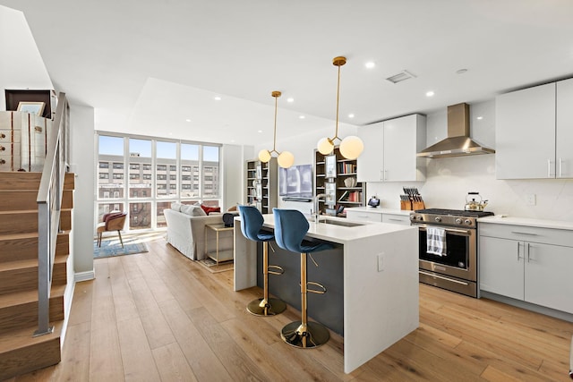 kitchen featuring stainless steel gas range, light wood-type flooring, wall chimney range hood, visible vents, and a sink