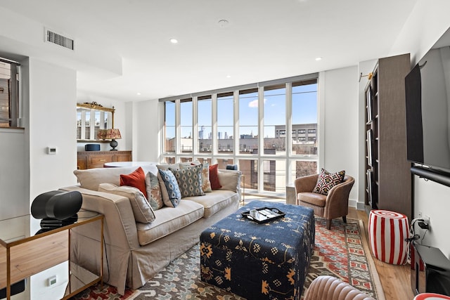 living room featuring a city view, expansive windows, visible vents, recessed lighting, and wood finished floors