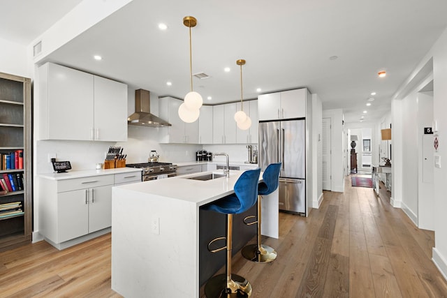 kitchen featuring a kitchen breakfast bar, wall chimney exhaust hood, premium appliances, light wood finished floors, and a sink