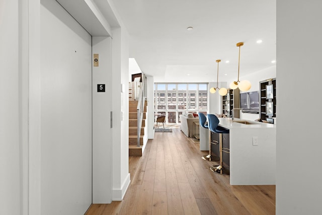 corridor with elevator, a sink, a wall of windows, recessed lighting, and light wood-style flooring