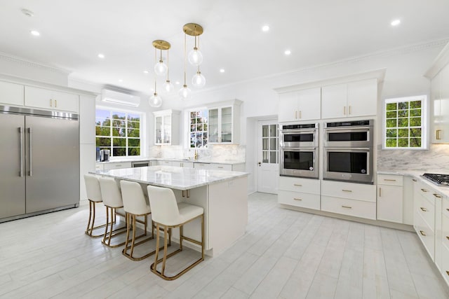 kitchen featuring white cabinetry, appliances with stainless steel finishes, hanging light fixtures, and an AC wall unit