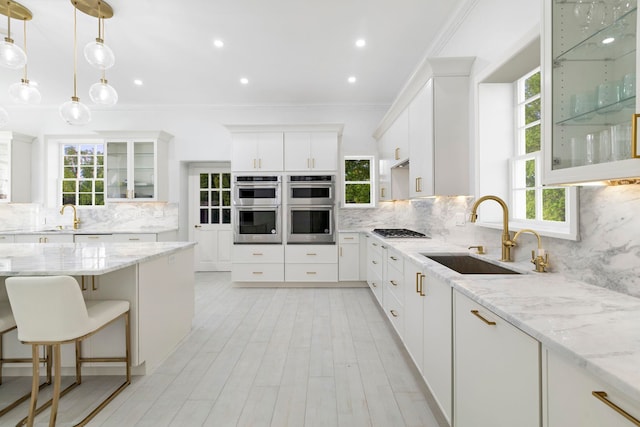 kitchen with stainless steel appliances, light stone counters, sink, backsplash, and white cabinetry