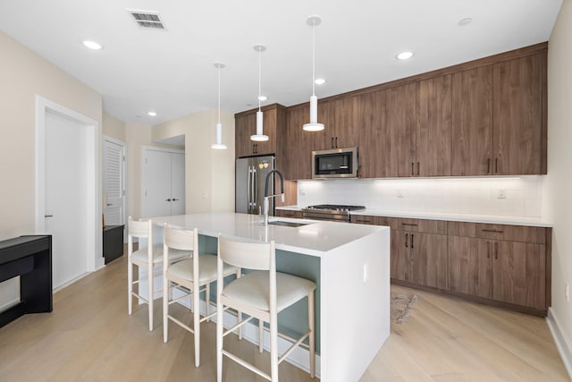 kitchen with a center island with sink, a breakfast bar, decorative light fixtures, stainless steel appliances, and light countertops