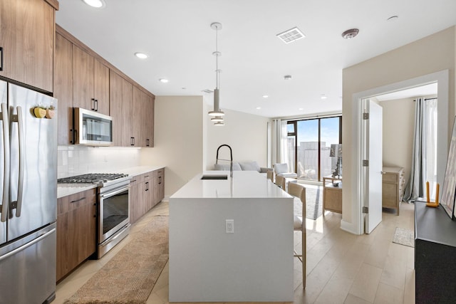 kitchen featuring decorative light fixtures, visible vents, light countertops, appliances with stainless steel finishes, and a kitchen island with sink