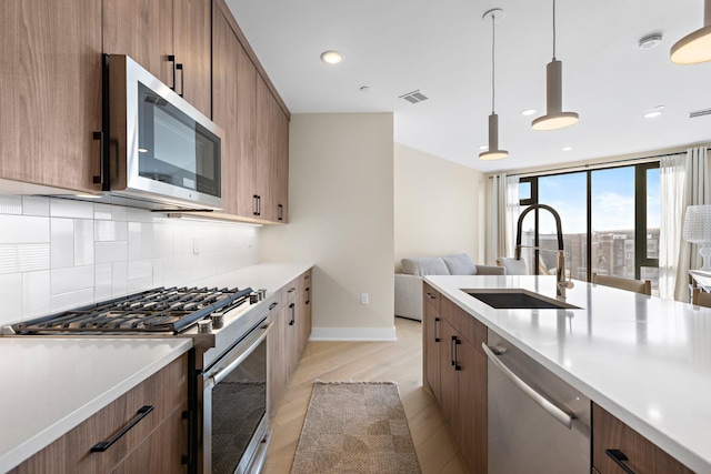 kitchen featuring pendant lighting, light countertops, decorative backsplash, appliances with stainless steel finishes, and a sink