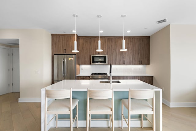 kitchen with stainless steel appliances, a kitchen island with sink, light countertops, and modern cabinets