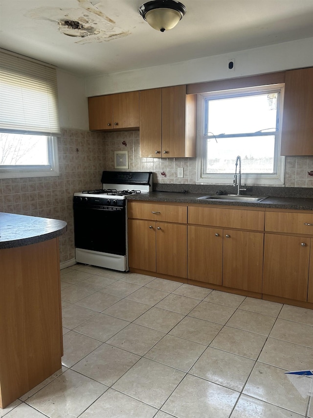 kitchen featuring a sink, range with gas stovetop, dark countertops, and light tile patterned flooring