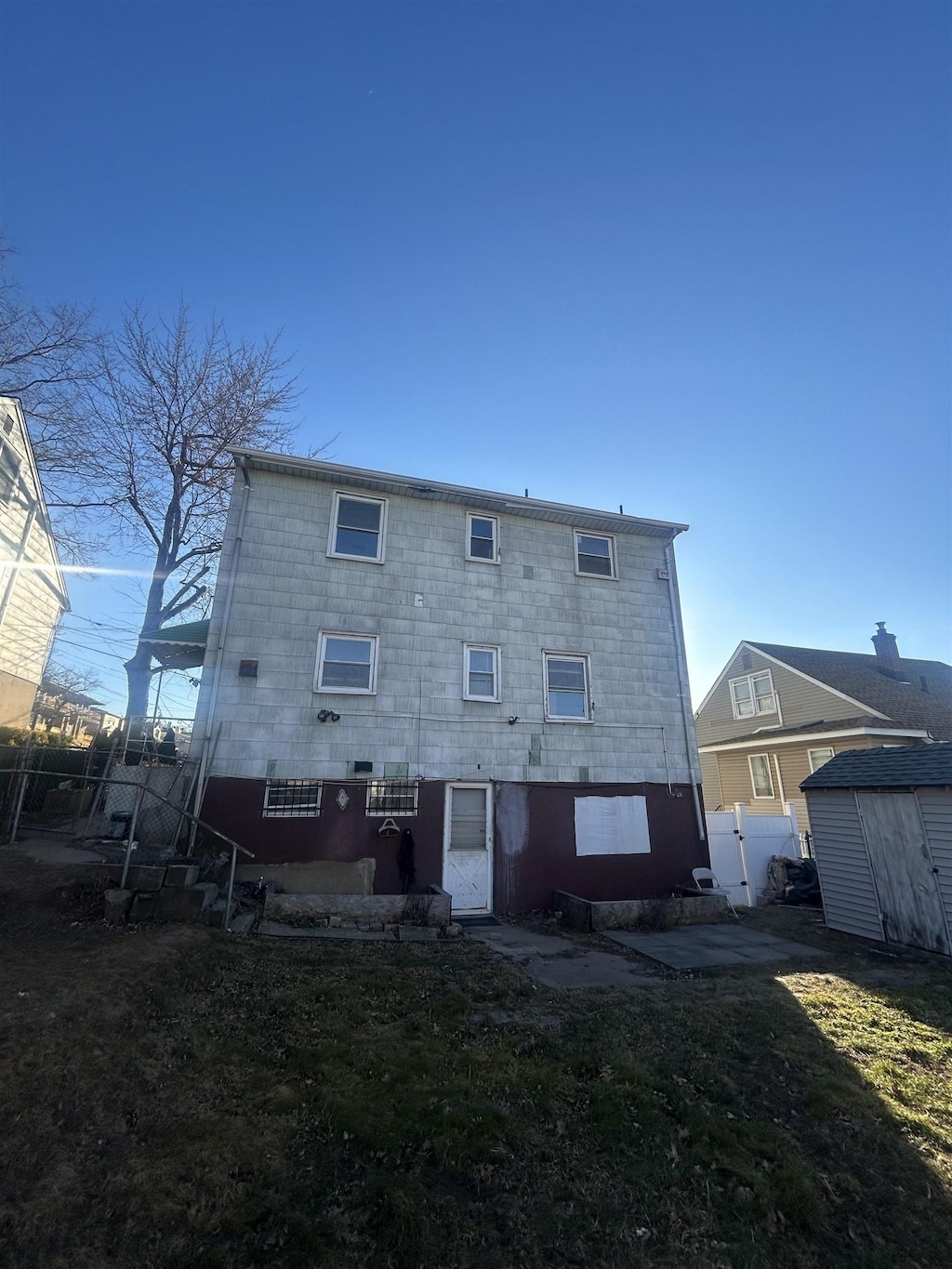 back of house with a storage unit, an outbuilding, a lawn, and fence